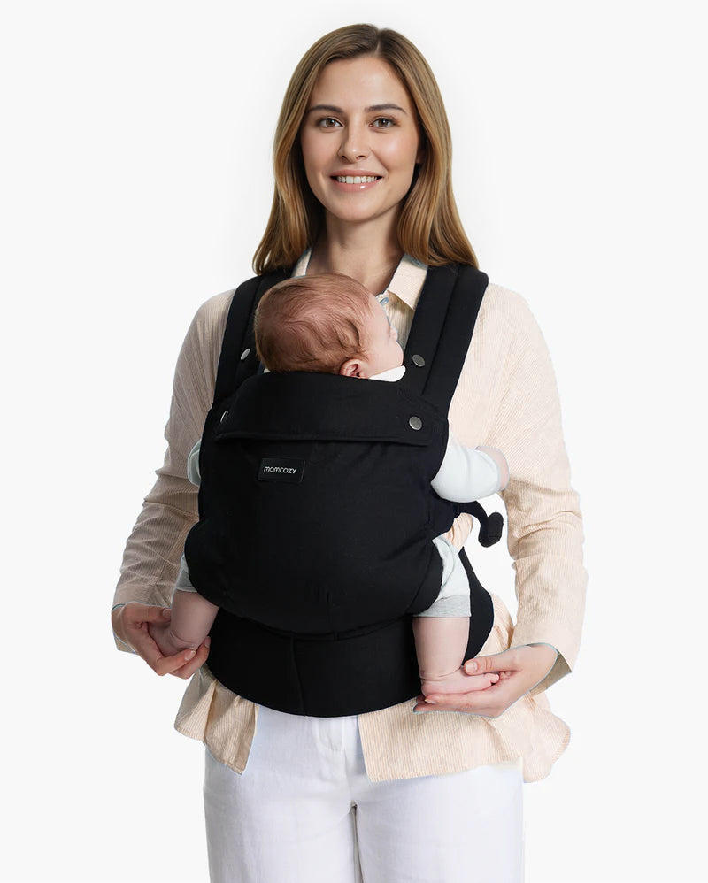 Momcozy PureHug Babytrage in Schwarz, von einer Frau mit Neugeborenem getragen